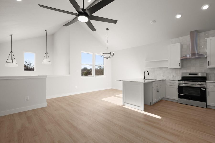 Kitchen with electric range, a peninsula, light wood-type flooring, decorative backsplash, and a chandelier