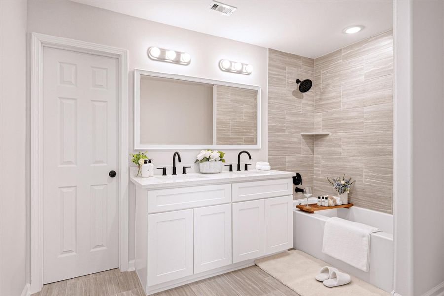 Primary bathroom. Spa-like retreat with a quartz-topped custom vanity with dual sinks. Beautiful tiles, elegant fixtures, and high-arc faucets. Indulge and relax in the upgraded bathtub after a long day of hard work. From a previous project with a similar floor plan