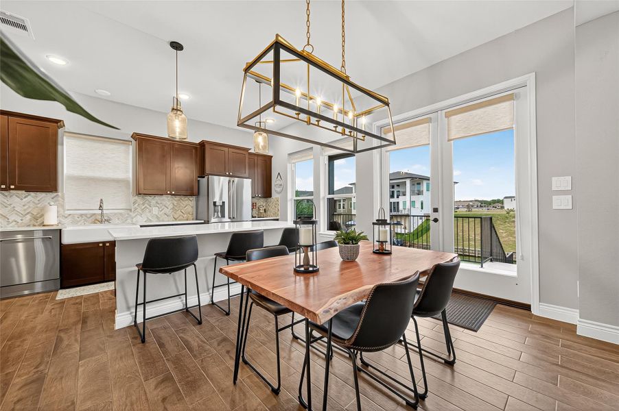 Open-concept kitchen featuring rich cabinetry, quartz countertops, herringbone backsplash, stainless-steel appliances, and a large island with bar seating. Dining area overlooks the lake through large windows and glass doors, creating a bright, relaxing atmosphere. Open-concept kitchen featuring rich cabinetry, quartz countertops, herringbone backsplash, stainless-steel appliances, and a large island with bar seating. Dining area overlooks the lake through large windows and glass doors, creating a bright, relaxing atmosphere.