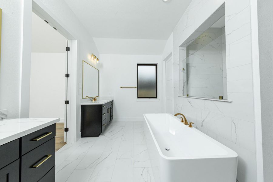 Modern primary bath features dual vanities with sleek dark cabinetry, a quartz countertop, framed vanity mirrors, and brushed gold fixtures for a truly contemporary feel.