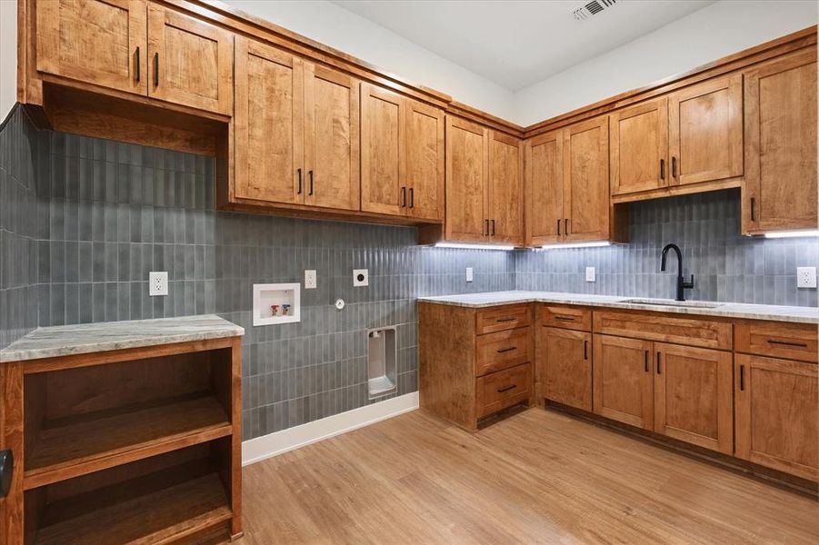 Kitchen featuring brown cabinets, light wood-type flooring, light stone counters, and tasteful backsplash