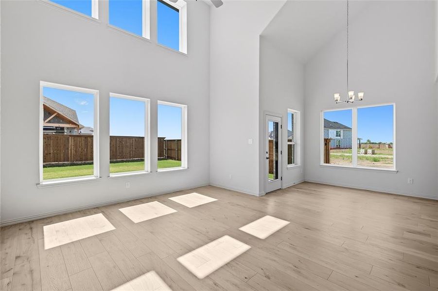 Unfurnished living room with a high ceiling, light wood-style floors, and a chandelier Unfurnished living room with a high ceiling, light wood-style floors, and a chandelier