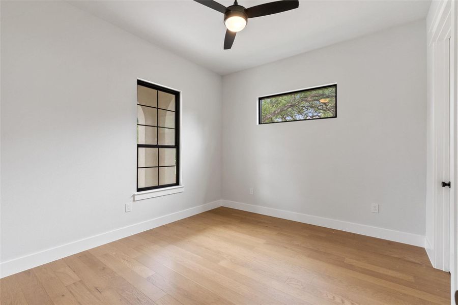 Blonde hardwood floors and a modern ceiling fan elevate this tranquil, naturally lit bedroom.