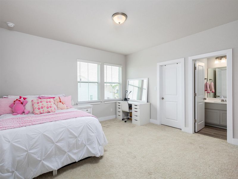 Bedroom with light colored carpet, a desk, and connected bathroom