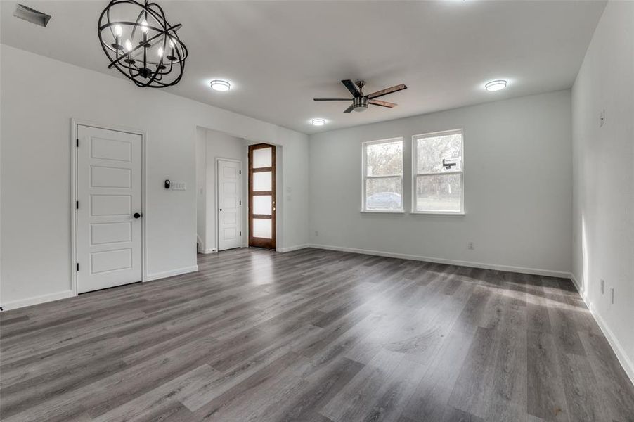 Unfurnished living room featuring ceiling fan with notable chandelier and dark wood-type flooring