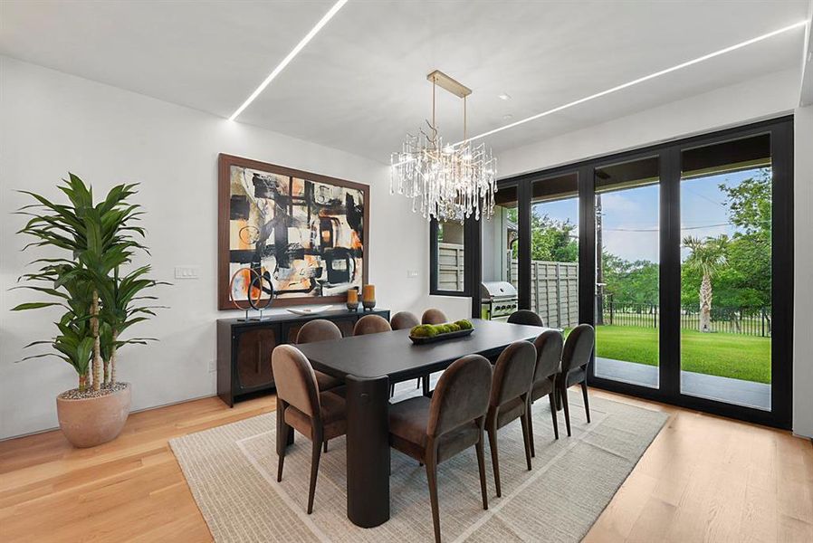 Dining area featuring large-format sliding glass doors, light wood-finish flooring, and recessed linear lighting