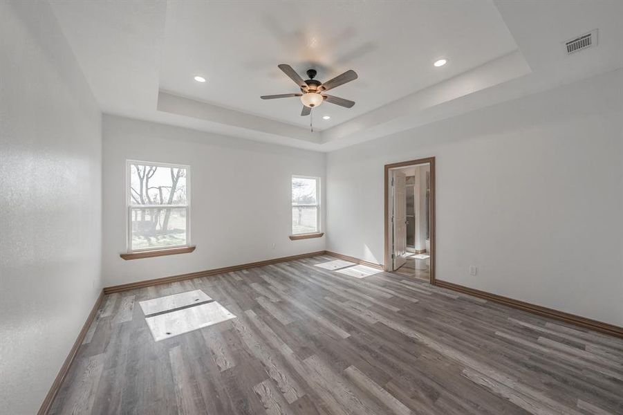 Unfurnished room featuring a tray ceiling, recessed lighting, visible vents, wood finished floors, and baseboards