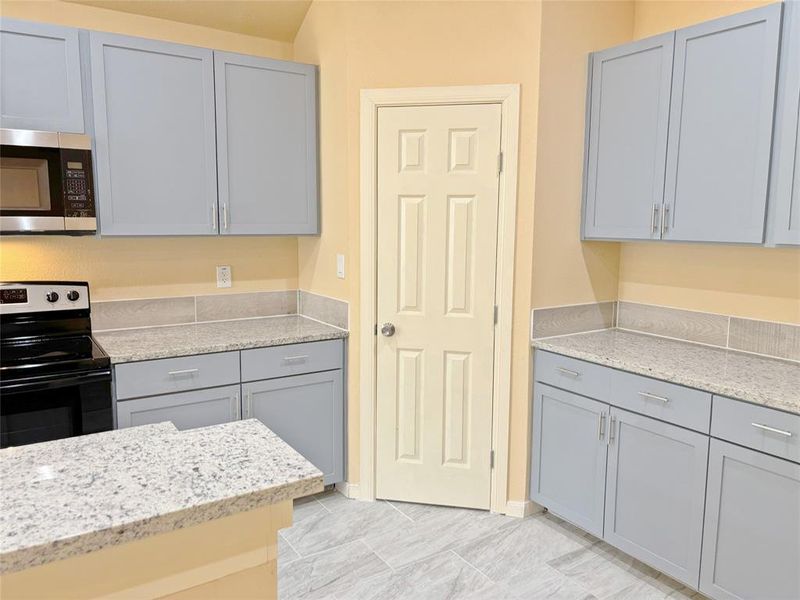 Kitchen featuring gray cabinetry, black range with electric cooktop, stainless steel microwave, and light stone countertops