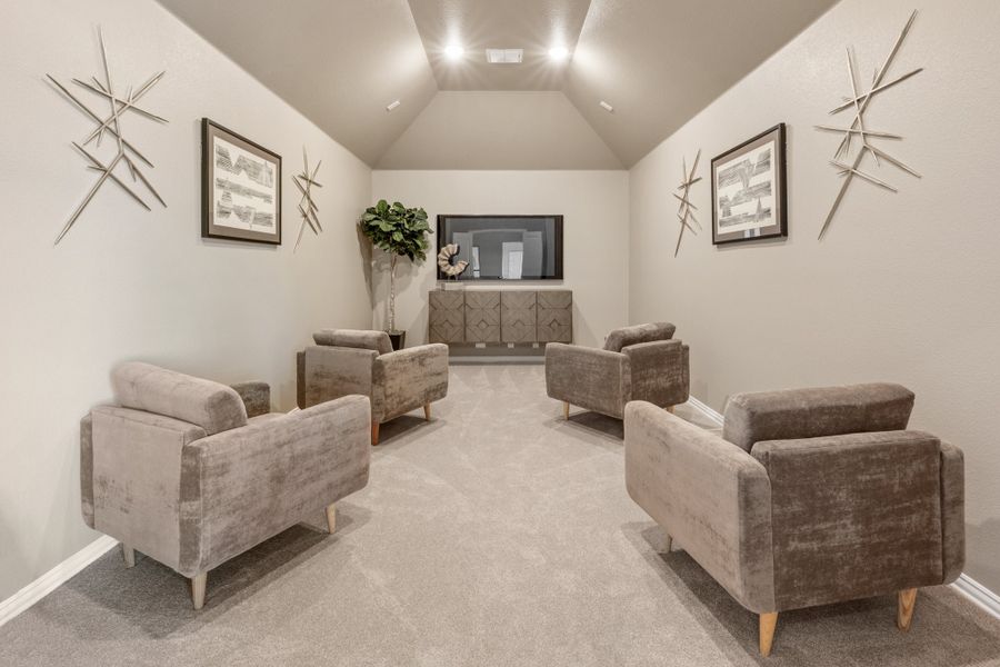 Sitting room with four gray armchairs, vaulted ceiling, wall art, and a TV console against the back wall.