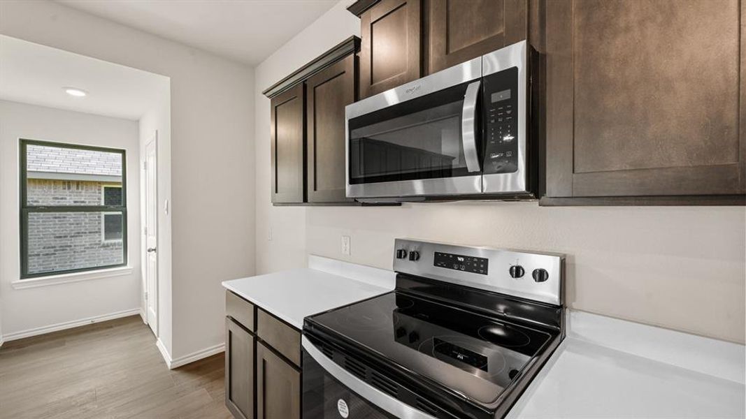Kitchen area featuring stainless steel appliances, dark wood cabinetry, and white countertops Kitchen area featuring stainless steel appliances, dark wood cabinetry, and white countertops