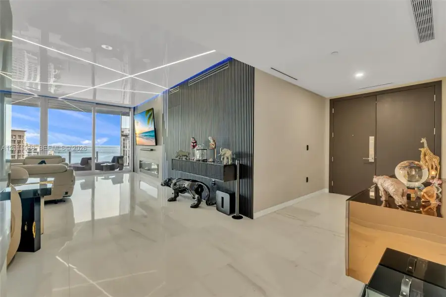 Living space featuring floor-to-ceiling glass sliding doors, high-gloss finish flooring, a linear built-in fireplace, and a textured, vertical-slat accent wall with integrated recessed lighting Living space featuring floor-to-ceiling glass sliding doors, high-gloss finish flooring, a linear built-in fireplace, and a textured, vertical-slat accent wall with integrated recessed lighting