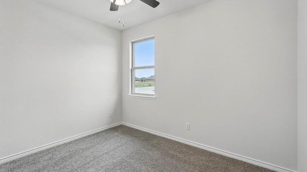 Room featuring a window, light gray walls, gray carpet flooring, white baseboards, and an overhead ceiling fan