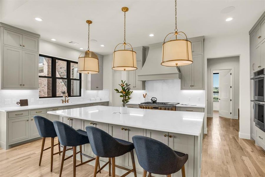Kitchen featuring gray cabinets, decorative light fixtures, a kitchen breakfast bar, decorative backsplash, and light wood finished floors Kitchen featuring gray cabinets, decorative light fixtures, a kitchen breakfast bar, decorative backsplash, and light wood finished floors