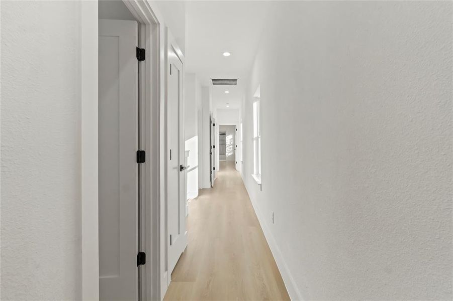 Hall featuring light wood finished floors, a textured wall, and recessed lighting