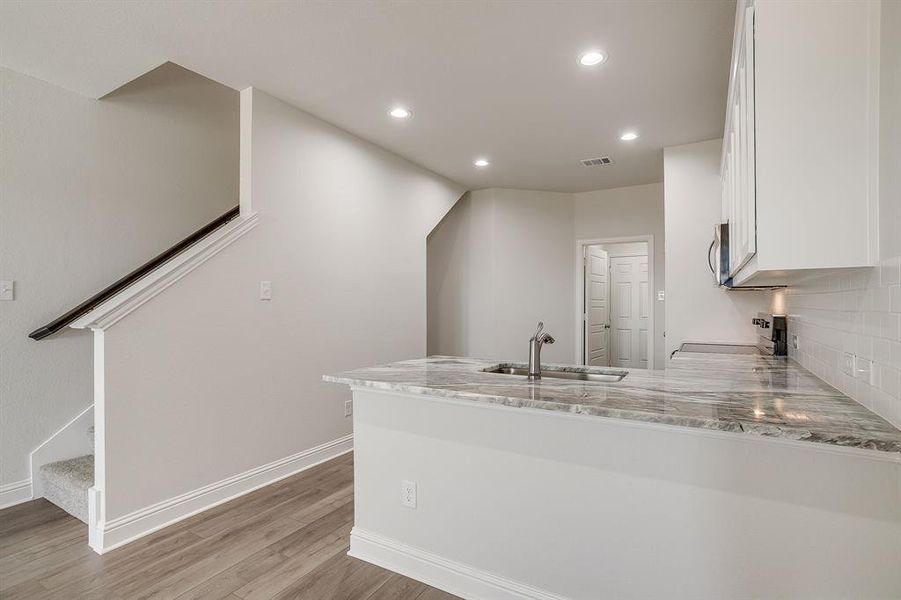 Kitchen with light stone countertops, a peninsula, recessed lighting, light wood finished floors, and black electric range oven