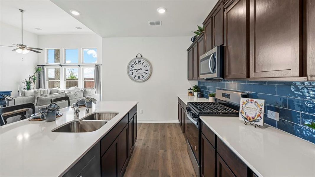 Contemporary kitchen featuring an island with a double basin sink, white countertops, dark wood-finish cabinetry, a subway tile backsplash, and stainless steel appliances