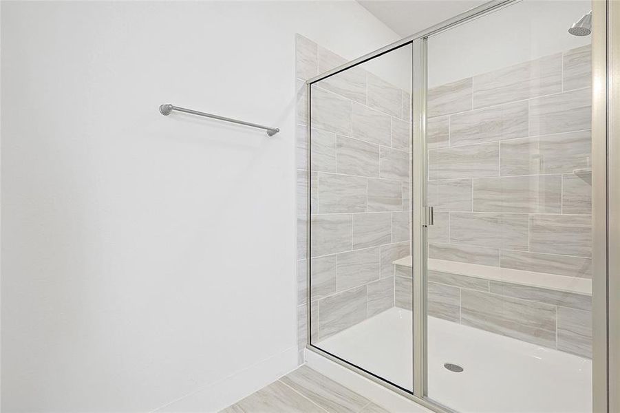 Modern shower with glass enclosure, light-toned tile walls, and an integrated bench