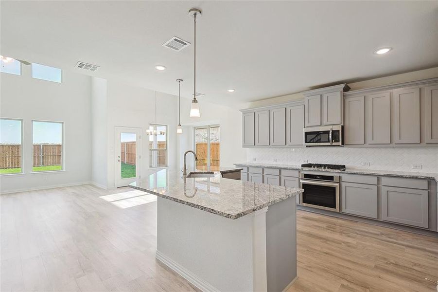 Kitchen with light stone counters, stainless steel appliances, sink, and a kitchen island with sink