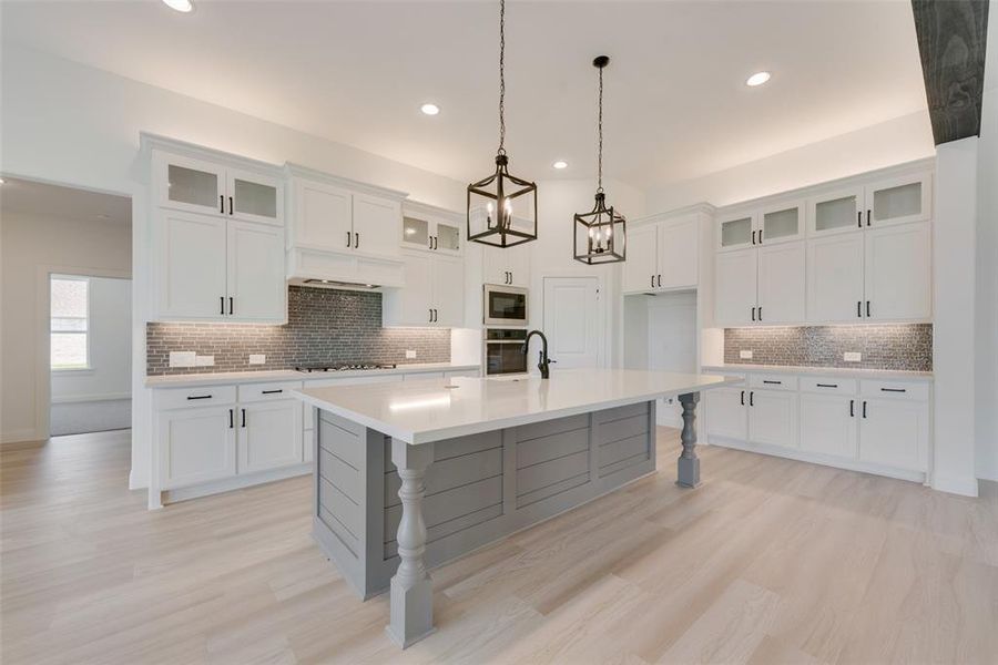 Kitchen featuring white cabinetry, backsplash, black appliances, and a center island with sink