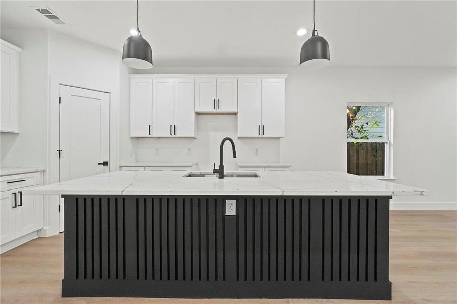 Kitchen featuring white cabinets, light wood-style floors, light stone countertops, a center island with sink, and recessed lighting Kitchen featuring white cabinets, light wood-style floors, light stone countertops, a center island with sink, and recessed lighting