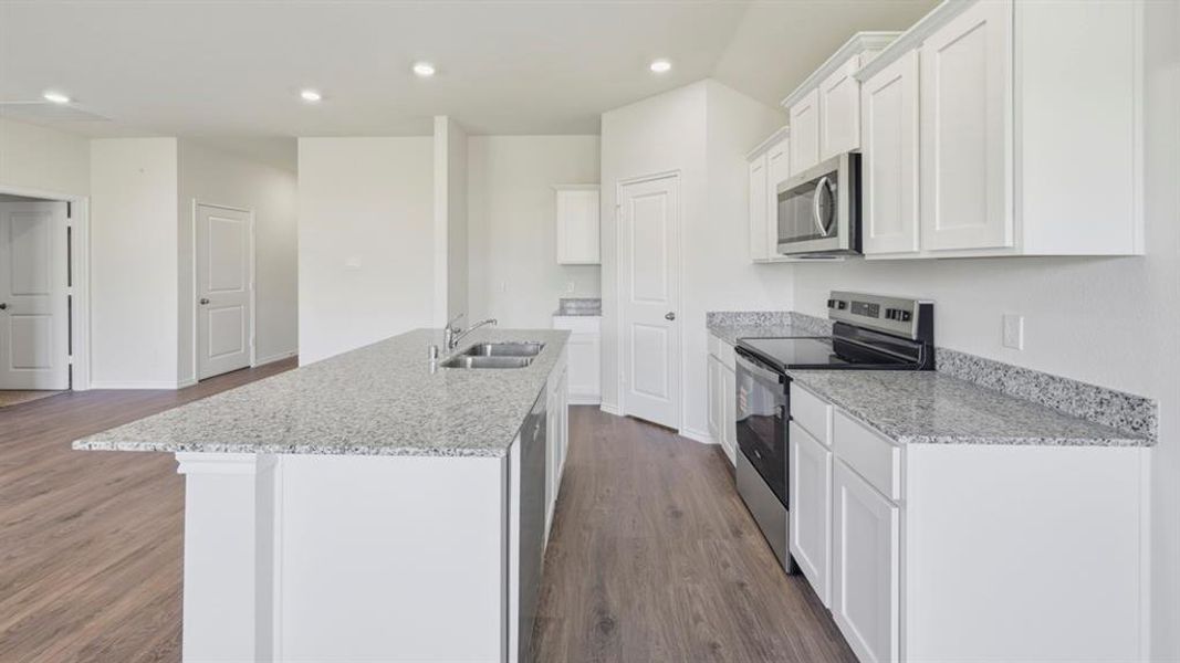 Kitchen with stainless steel appliances, dark wood-type flooring, white cabinetry, light stone counters, and an island with sink Kitchen with stainless steel appliances, dark wood-type flooring, white cabinetry, light stone counters, and an island with sink