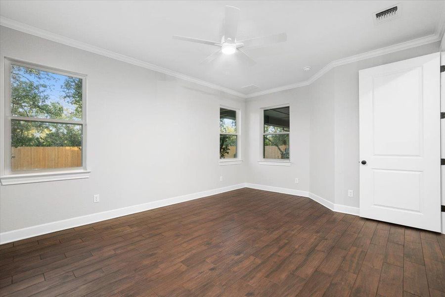 Empty room with plenty of natural light, dark wood-type flooring, a ceiling fan, baseboards, and crown molding Empty room with plenty of natural light, dark wood-type flooring, a ceiling fan, baseboards, and crown molding