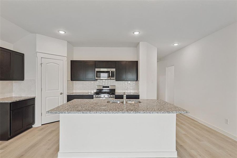 Kitchen with light hardwood / wood-style flooring, decorative backsplash, stainless steel appliances, and a center island with sink