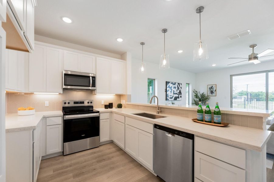 Kitchen with stainless steel appliances, a peninsula, white cabinetry, light wood-style flooring, and tasteful backsplash