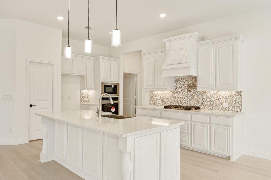 White kitchen with large island, pendant lights, mosaic tile backsplash, and stainless steel appliances White kitchen with large island, pendant lights, mosaic tile backsplash, and stainless steel appliances