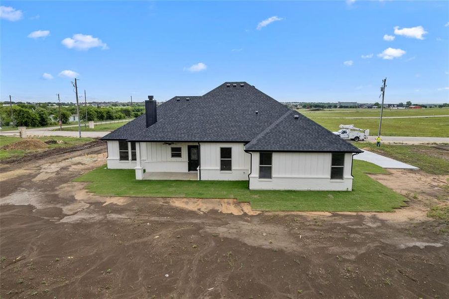 Rear view of property with a chimney, a shingled roof, a lawn, and a patio