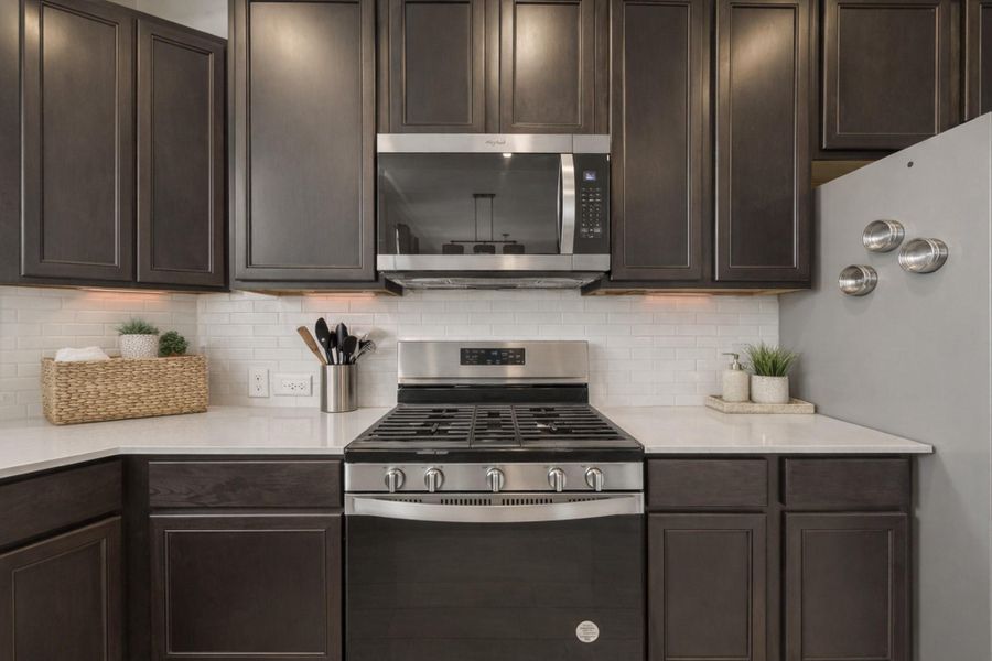 Sleek U-shaped kitchen with rich cabinetry, quartz counters, and crisp subway-tile backsplash.