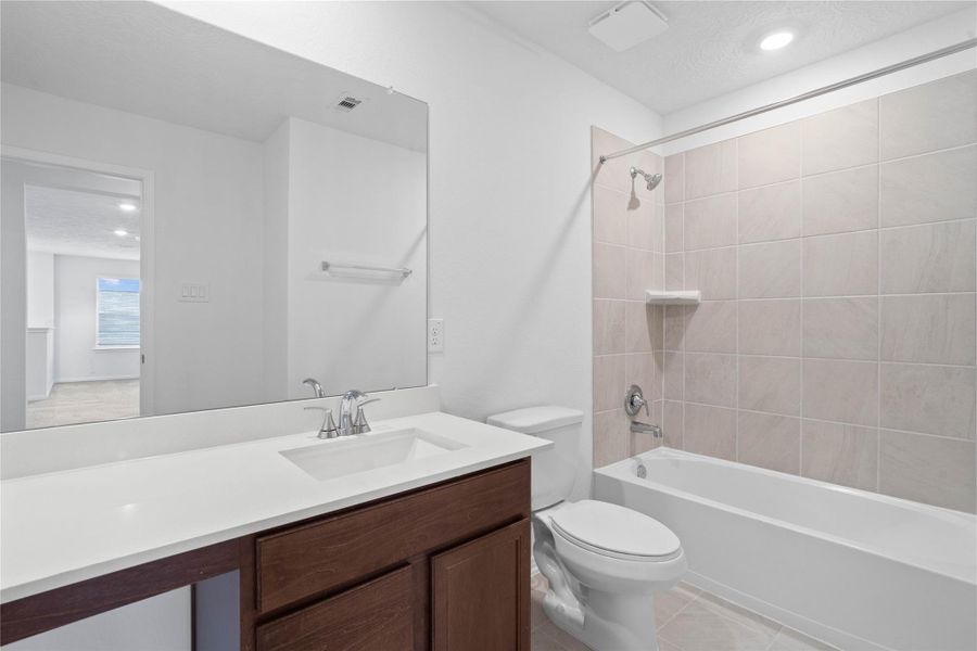 The secondary bathroom showcases tile flooring, a bath/shower combo with tile surround, a vanity with knee space and stunning light countertop, a mirror, sleek fixtures, and contemporary finishes throughout.