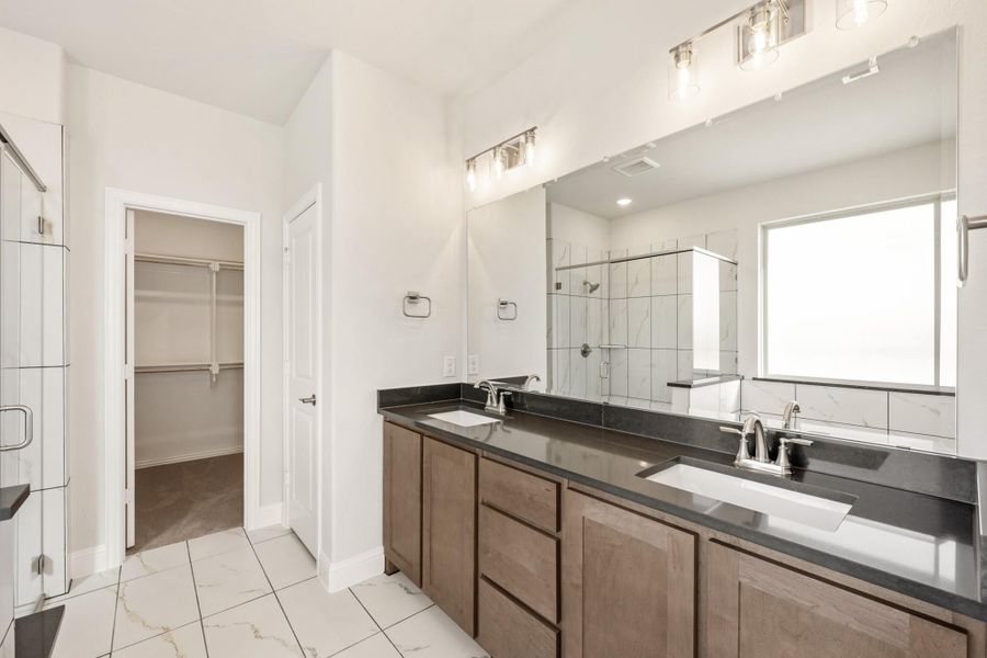 Bathroom with double vanity, dark countertops, walk-in closet, and tiled shower with glass door Bathroom with double vanity, dark countertops, walk-in closet, and tiled shower with glass door