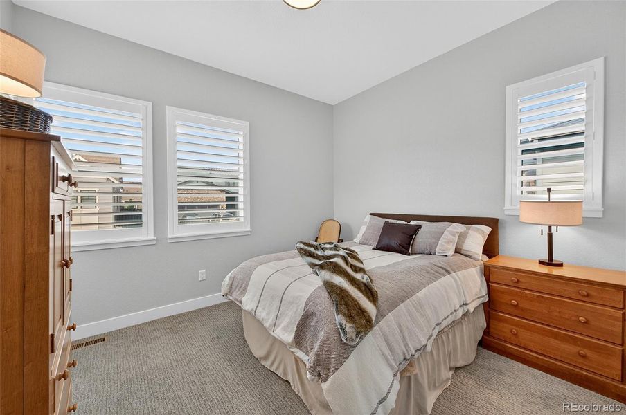 Bedroom 2 (Angle 1) – Bright and comfortable secondary bedroom featuring neutral tones, large windows with plantation shutters, and plush carpet flooring.
