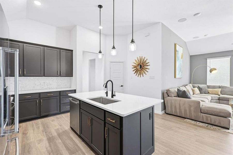 Kitchen featuring open floor plan, vaulted ceiling, light wood finished floors, a center island with sink, and pendant lighting