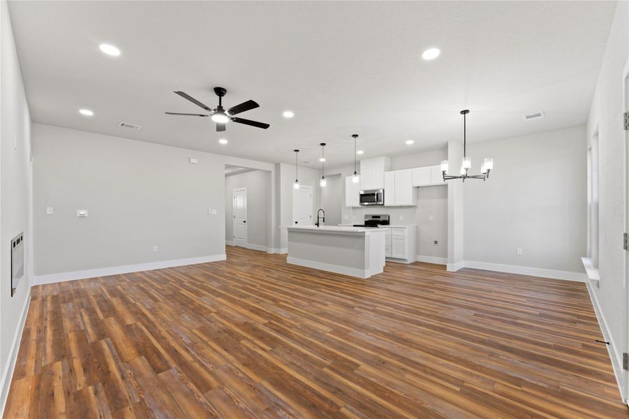 Unfurnished living room with ceiling fan, suspended lighting, and dark wood-style floors