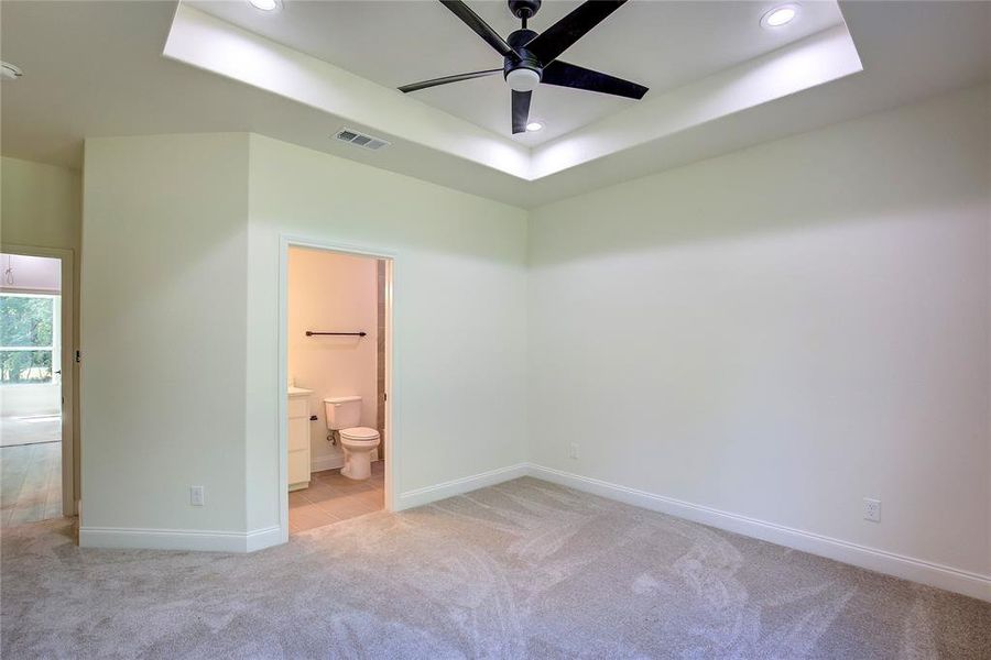 Unfurnished bedroom with light colored carpet, recessed lighting, ensuite bath, and a raised ceiling Unfurnished bedroom with light colored carpet, recessed lighting, ensuite bath, and a raised ceiling