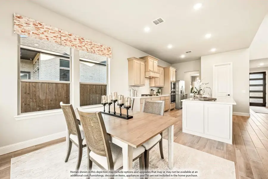 Open dining area with wood table and chairs flowing into kitchen with light wood cabinets and white island