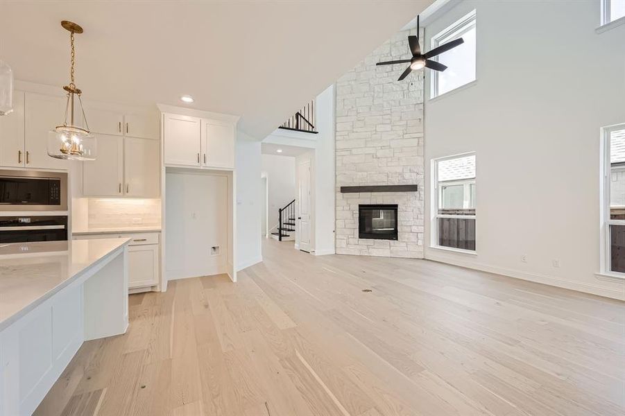 Kitchen featuring white cabinetry, oven, a stone fireplace, a high ceiling, and ceiling fan