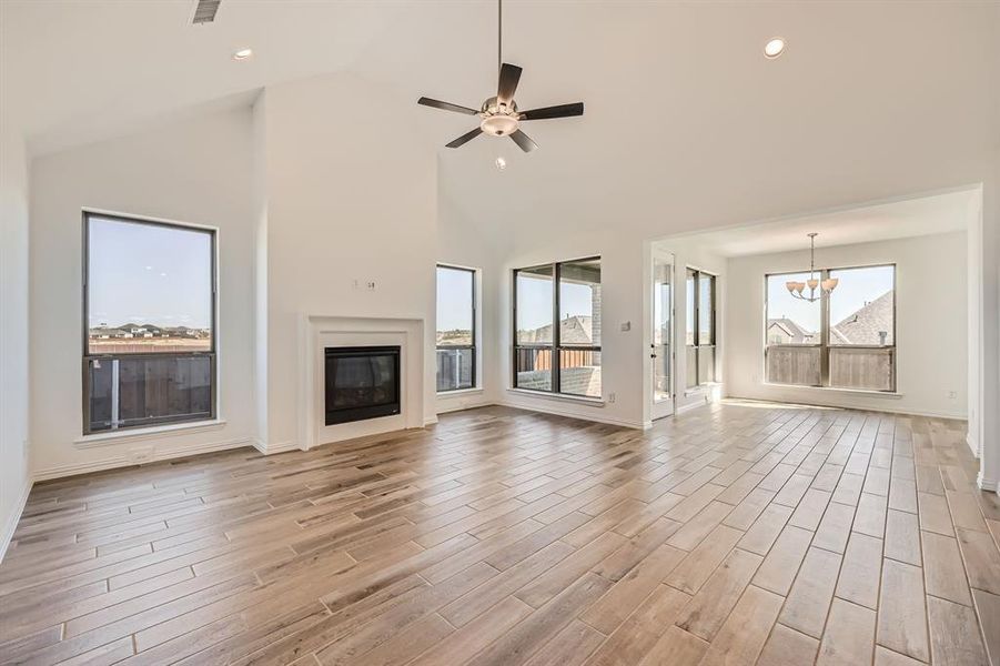 Unfurnished living room with ceiling fan with notable chandelier, light wood-type flooring, and high vaulted ceiling