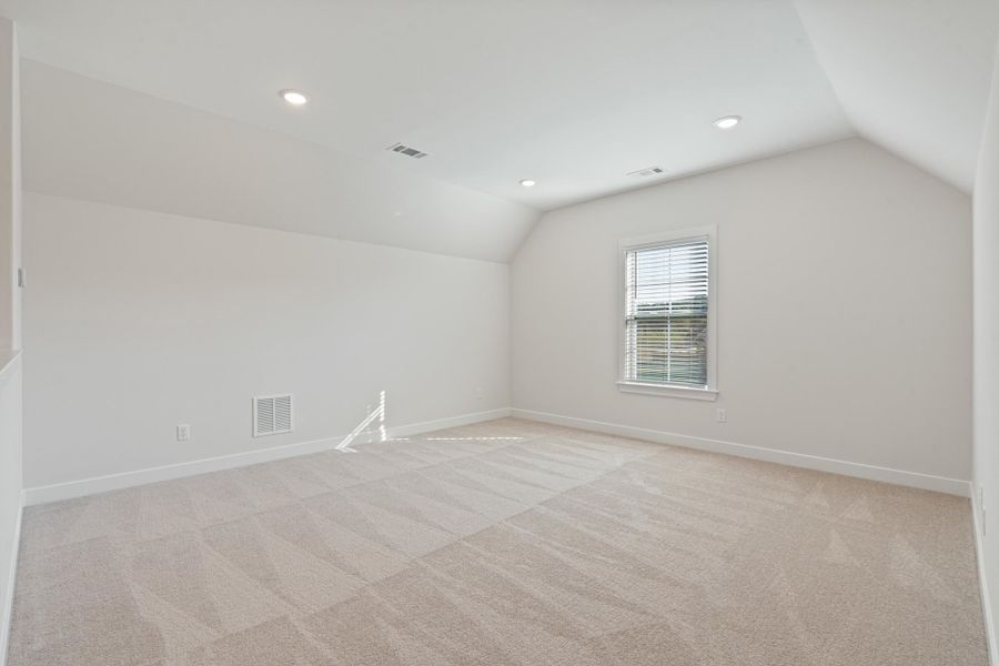 Spacious room featuring vaulted ceilings, recessed lighting, neutral carpeting, and a window with blinds