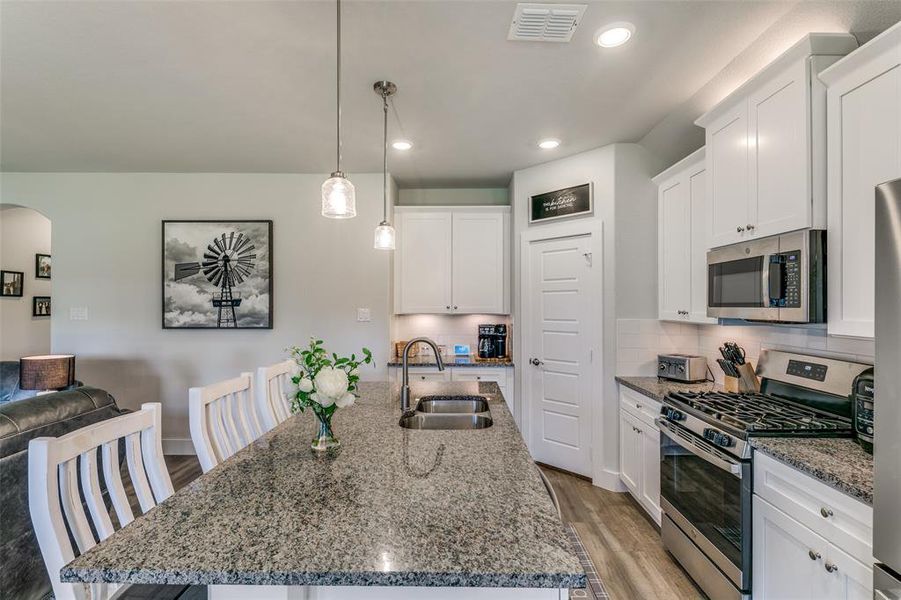 Kitchen featuring light hardwood / wood-style floors, a kitchen island with sink, sink, hanging light fixtures, and appliances with stainless steel finishes