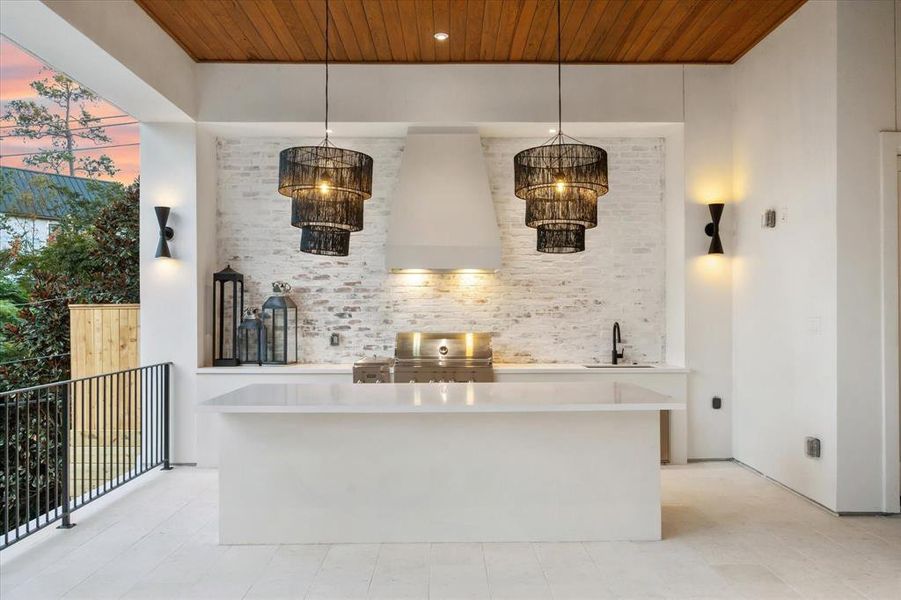 This luxury summer kitchen is designed for ultimate convenience, making it ideal for catering or entertaining with your personal chef. A stunning brick accent wall ties the exterior together beautifully, while dual designer light fixtures add an elegant touch to the space.