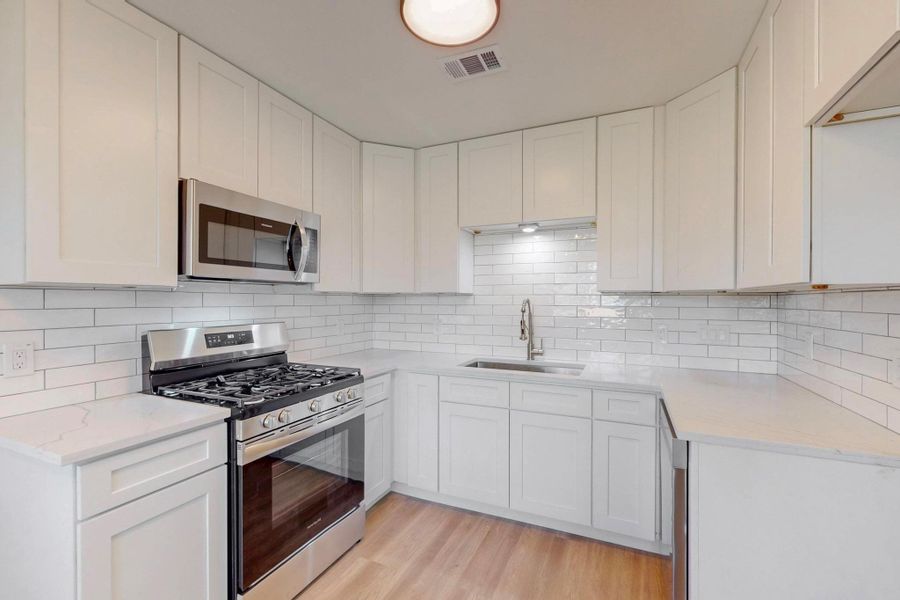 Kitchen with white cabinetry, light stone countertops, visible vents, appliances with stainless steel finishes, and a sink