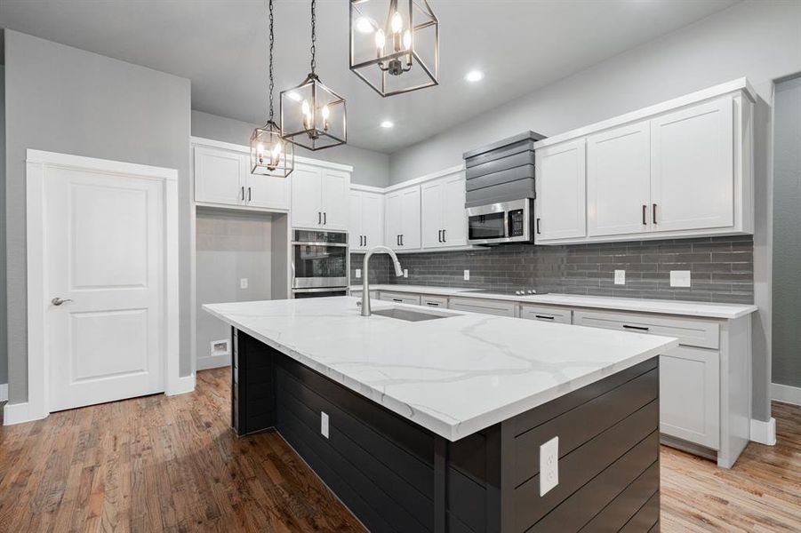 Kitchen with appliances with stainless steel finishes, an inviting chandelier, a sink, light wood finished floors, and tasteful backsplash Kitchen with appliances with stainless steel finishes, an inviting chandelier, a sink, light wood finished floors, and tasteful backsplash