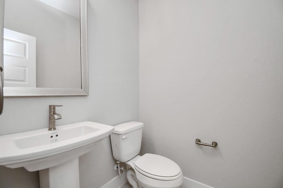 A glimpse of the spacious upgraded half bath featuring a pedestal sink, sophisticated light fixtures, and sleek hardware. Sample photo of completed home with similar floor plan. Actual colors and selections may vary. A glimpse of the spacious upgraded half bath featuring a pedestal sink, sophisticated light fixtures, and sleek hardware. Sample photo of completed home with similar floor plan. Actual colors and selections may vary.