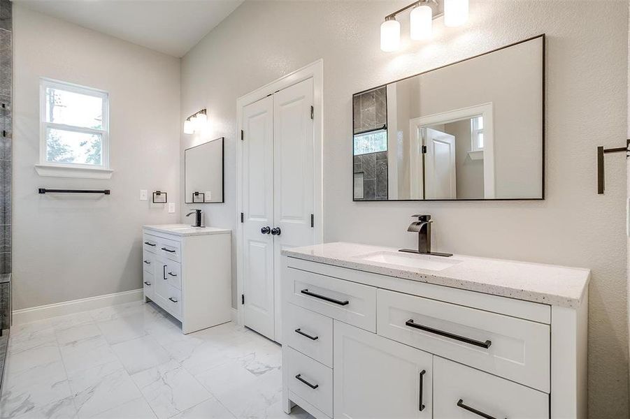 Bathroom featuring marble finish floor, baseboards, tiled shower, two vanities, and a sink Bathroom featuring marble finish floor, baseboards, tiled shower, two vanities, and a sink