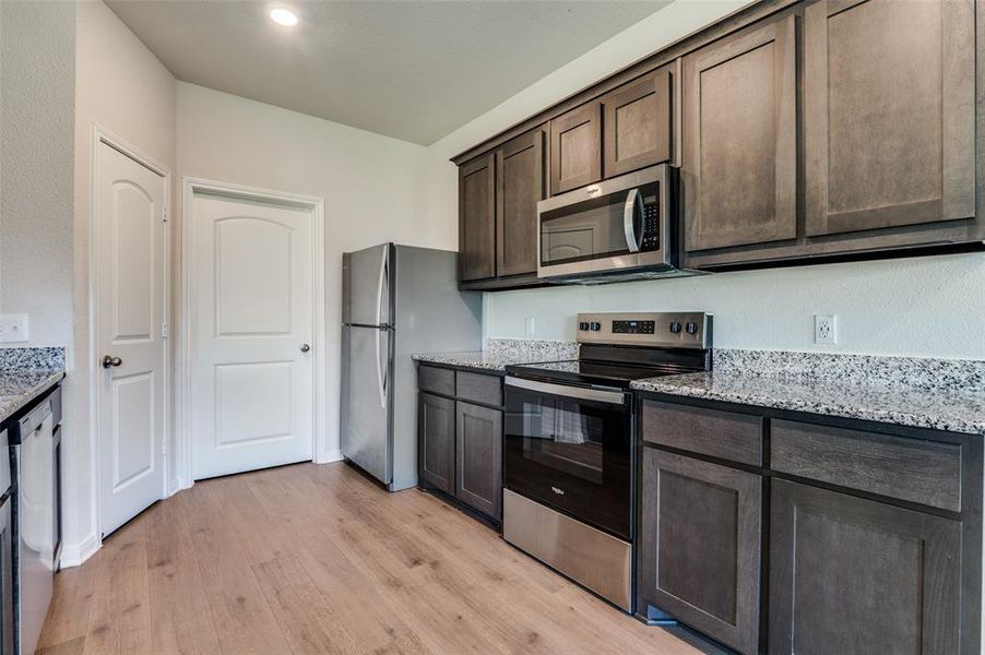 Kitchen with stainless steel appliances, light stone countertops, dark wood finish cabinetry, and light wood-type flooring