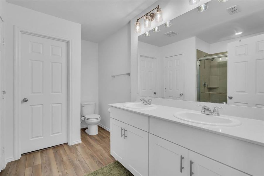 Bathroom featuring a stall shower, double vanity, and light wood-type flooring