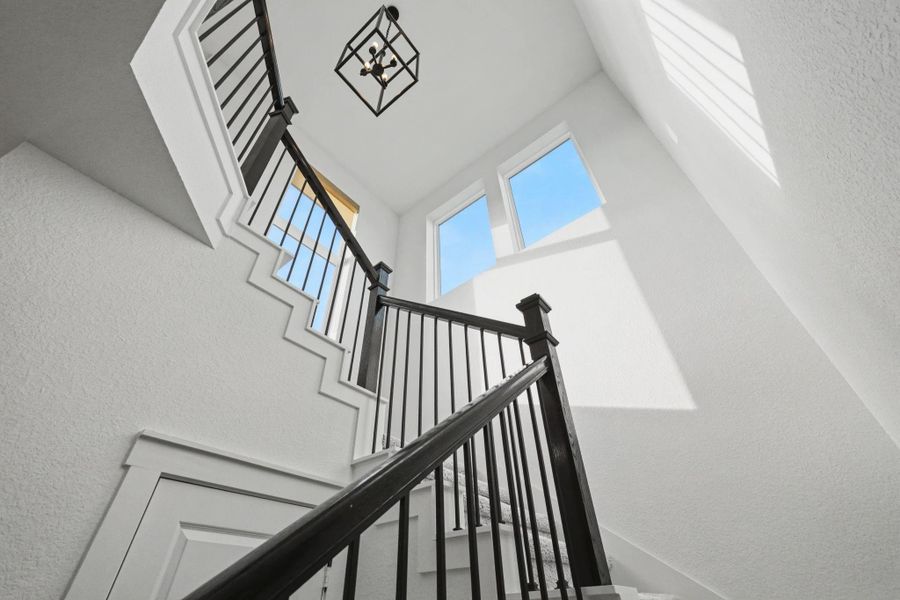 Dramatic stairwell highlighted by soaring ceilings, oversized windows, and modern iron railing. Sunlight pours through the upper windows, creating a bright architectural focal point and an impressive sense of openness.